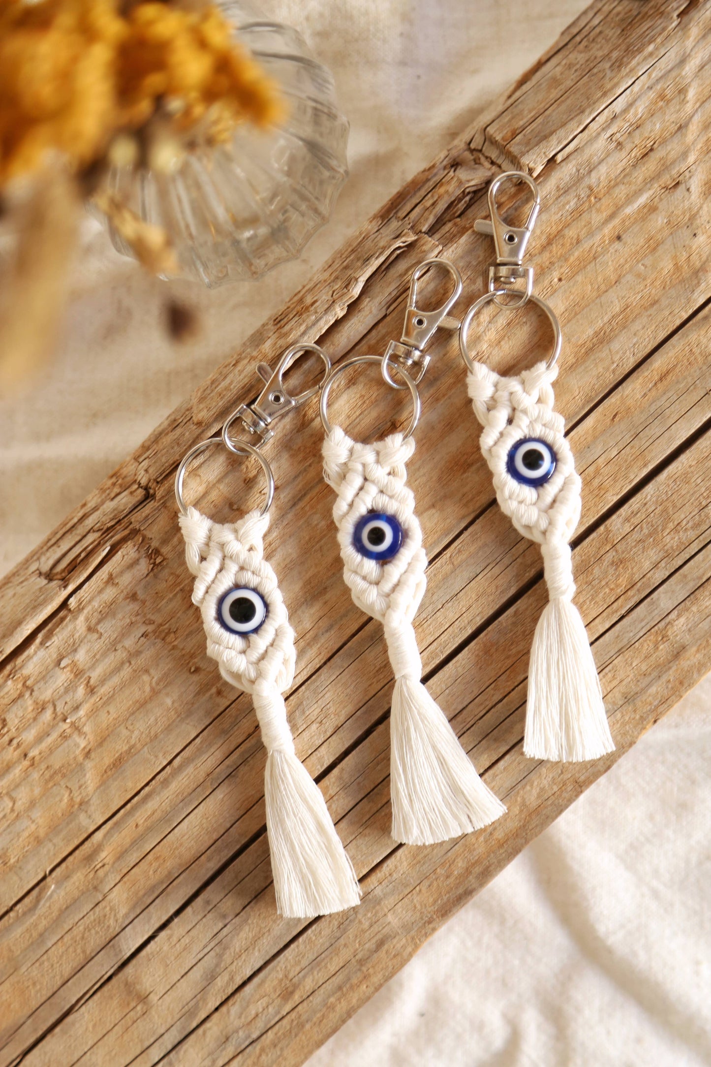 Three macrame keychains with evil eye design on a wooden surface.